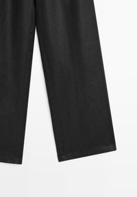 Czarne lniane spodnie o szerokich nogawkach, charakteryzujące się gładką fakturą i czystymi, obszytymi krawędziami. Prosty, nieskomplikowany wygląd.