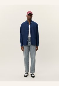 Navy button-up shirt, white t-shirt underneath, light blue jeans, black and white shoes, and a maroon baseball cap. Simple, casual outfit.