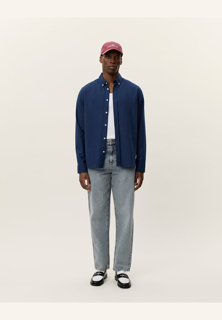 Navy button-up shirt, white t-shirt underneath, light blue jeans, black and white shoes, and a maroon baseball cap. Simple, casual outfit.