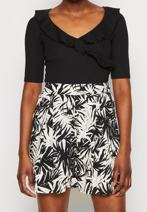 Black short-sleeve top features a v-neck and ruffled neckline; paired with high-waisted shorts in a black and white leaf pattern.