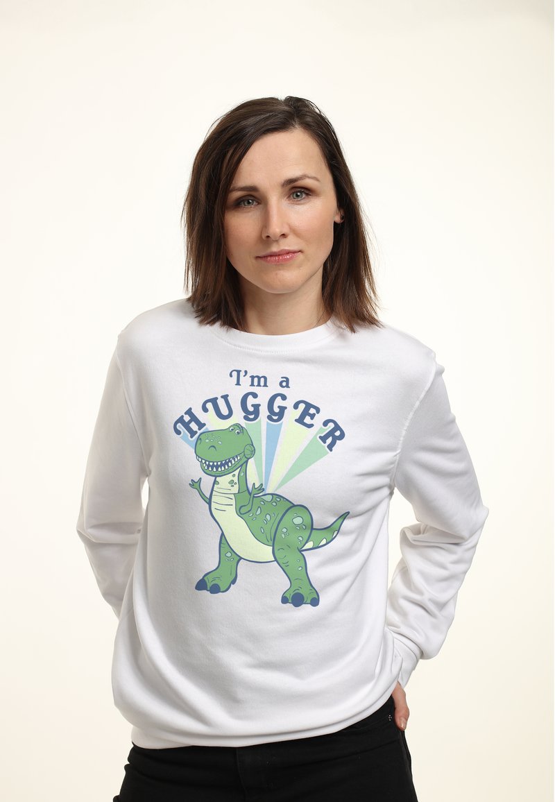 Sudadera blanca con un dinosaurio de dibujos animados verde y el texto "Soy un ABRAZADOR", sobre un fondo claro. Tejido suave, corte casual.