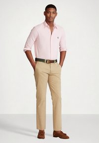 Ροζ πουκάμισο με κουμπιά, μπεζ chinos, καφέ ζώνη με πράσινες και μπλε λεπτομέρειες και καφέ loafers. Ομαλό ύφασμα και προσαρμοσμένη εφαρμογή.