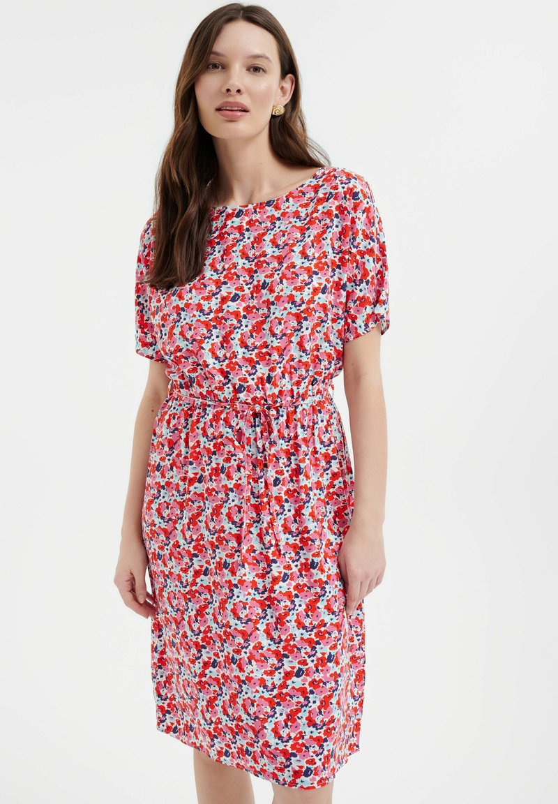 Blumenkleid mit losem Schnitt, kurzen Ärmeln, tailliertem Bund und einem lebendigen Muster aus roten, rosa und blauen Blumen auf hellem Hintergrund.