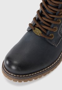 Bottine en cuir noir avec une surface texturée, des lacets marron contrastants, et une semelle en caoutchouc robuste avec des motifs de crampons visibles.