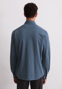 Langarmshirt van een gedempt blauwe stof, met een klassieke kraag, een gebogen onderrand en met knopen afsluitbare manchetten. Gladde textuur, minimalistisch ontwerp.