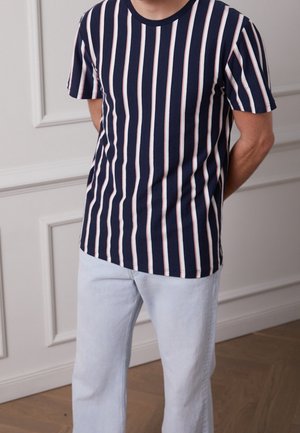 Marineblaues T-Shirt mit Rundhalsausschnitt und vertikalen weißen und pinkfarbenen Streifen, kombiniert mit hellblauen Jeans mit geradem Bein. Glatte Stoffstruktur.