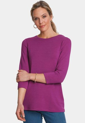 Fuchsia lange mouwen top met een ronde halslijn en een gladde textuur. Draagt bij blauwe jeans en een gouden kettingarmband.