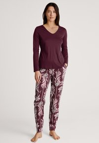 Bordeaux lange mouw top met V-hals, gecombineerd met gebloemde pyjamabroek in bordeaux met lichte bloemmotieven en maansikkels.