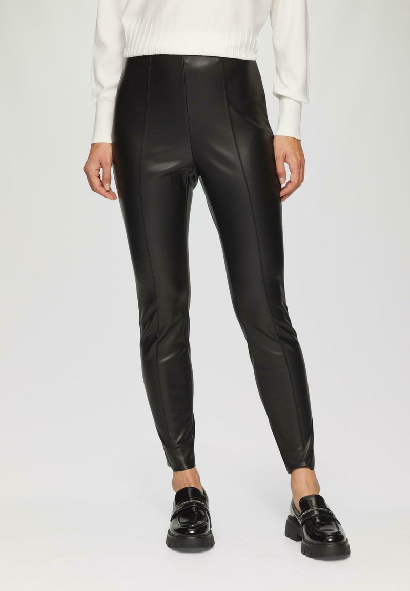 Mustad kunstnahk leggings kõrge vöökohaga, siledast tekstuurist ja külgmiste õmblustega, koos läikivate mustade loafersitega.