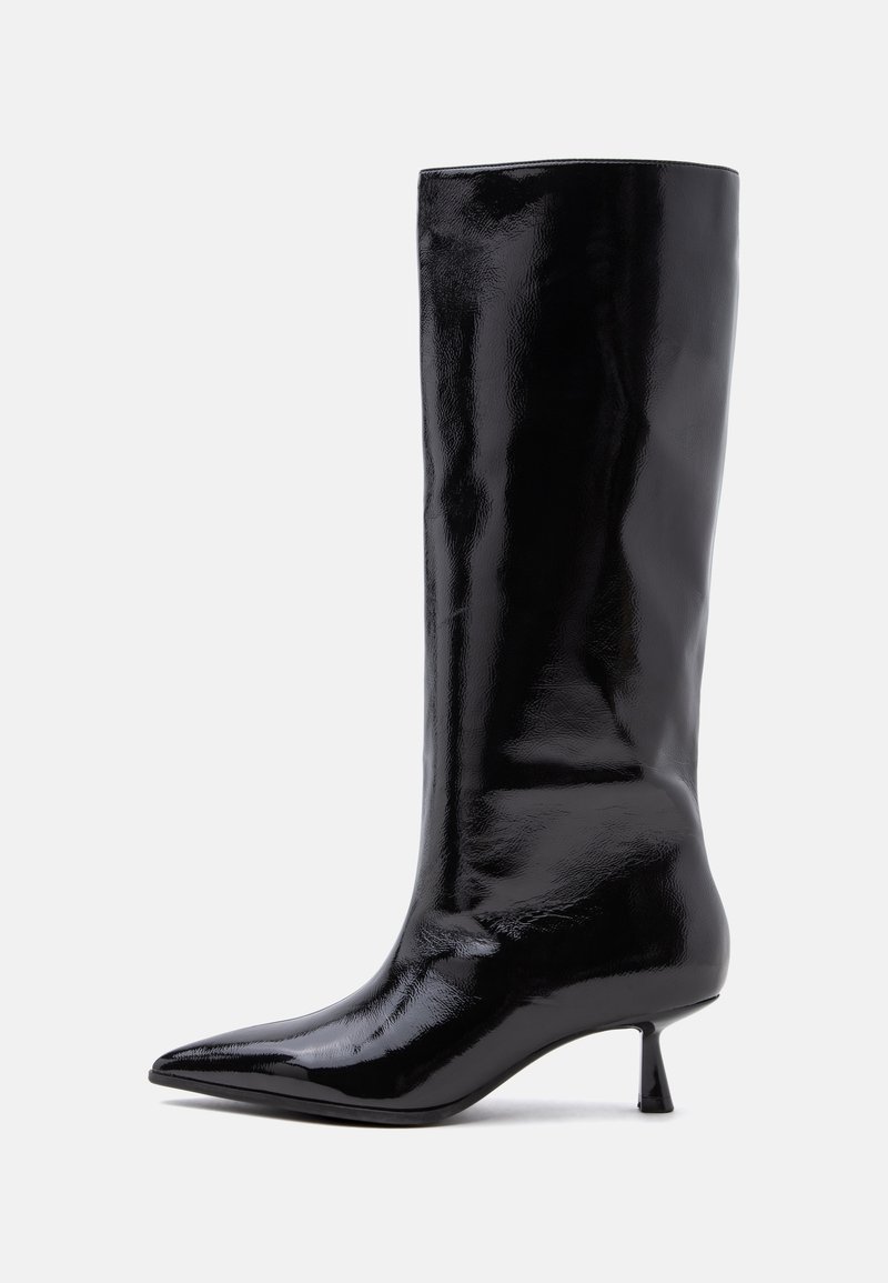 Botte noire brillante montant au genou avec bout pointu et petit talon kitten sur fond clair uni.