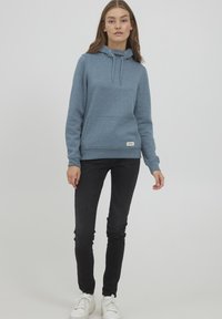 Blå huvtröja med dragsko, känguruficka och ribbade ärmslut, i kombination med svarta slim-fit jeans och vita sneakers.