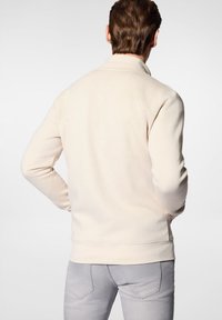 Kremowy polar w kolorze białym z wysokim kołnierzem, długimi rękawami i ściągaczem na dole. Wykonany z miękkiego, strukturalnego materiału. Minimalistyczny design.