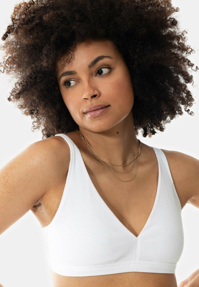 Witte geribbelde bralette met een diepe V-halsontwerp, voorzien van brede schouderbanden. Glad textuur zonder padding of baleinen.