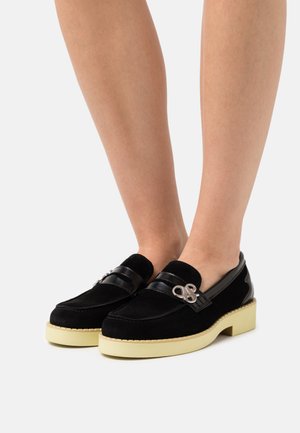 Black suede loafers with a shiny black leather band, silver hardware detail, and a chunky cream platform sole.