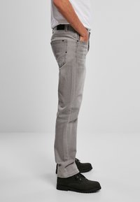 Jean gris de denim con corte recto, que presenta bolsillos laterales y herrajes negros. Llevados con botas ankle negras, mostrando un diseño simple.