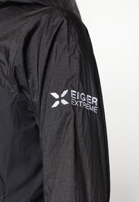 Melna jaka ar teksturētu apdari. Izšūts "EIGER EXTREME" logo baltā krāsā kreisajā piedurknē. Viegls materiāls, paredzēts āra lietošanai.