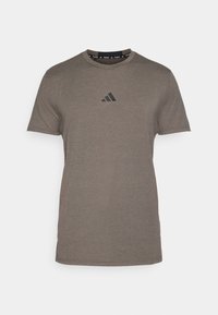 Brown short-sleeve t-shirt made of soft fabric, featuring a black Adidas logo on the chest and a round neck with logo accents.