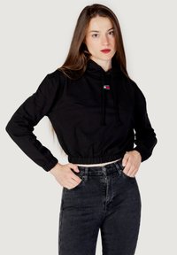 Felpa nera corta con cappuccio e lacci, polsini a coste e orlo elastico. Indossata sopra jeans neri a vita alta. Presenta un piccolo logo sul petto.