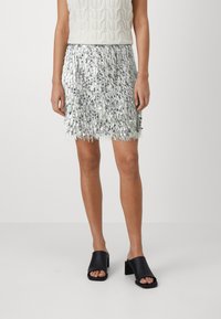 Jupe en sequins argentés avec une texture frangée, mi-longue. Associée à des sandales noires à talons carrés. Matériau léger et réfléchissant.