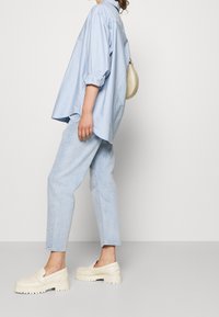 Jasnoniebieska, luźna koszula na guziki, jasnoniebieskie dżinsy oraz kremowe chodaki z grubą podeszwą. Mała kremowa torebka przewieszona przez ramię.