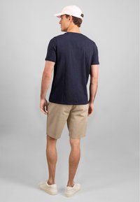 Marine t-skjorte, beige shorts, lyse sneakers og en rosa caps. Antrekket har en avslappet passform og minimalistisk design.