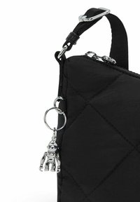 Angolo di una borsa trapuntata nera con tracolla regolabile, zip argentata e portachiavi a forma di robot argentato attaccato all'anello laterale.