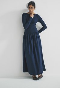 Mörkblå långärmad klänning med figursydd överdel och rynkad kjol. Tillverkad av mjukt tyg, har rundad halsringning och sömlös design.