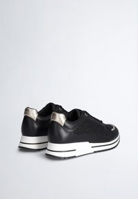 Schwarze Sneaker mit einem Mesh-Design, Lederakzenten und metallischem Absatz. Sie verfügen über eine weiße Sohle mit einem geschichteten Effekt und schwarzem Profil.