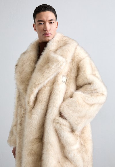 Šviesiai ruda dirbtinio kailio striukė su plačiu apykakle ir dideliu siluetu. Savybė - sidabro kvadratinis užsegimas ir minkšta, tekstūruota medžiaga.