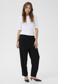 Pantaloni neri a gamba larga con tasche frontali, abbinati a una maglietta bianca aderente a maniche corte. Il modello indossa mules nere con tacco.