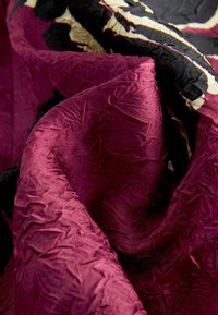 Samet stof in diep bordeaux met zwarte en crèmekleurige accenten, met een gekreukt textuur en een gladde glans.