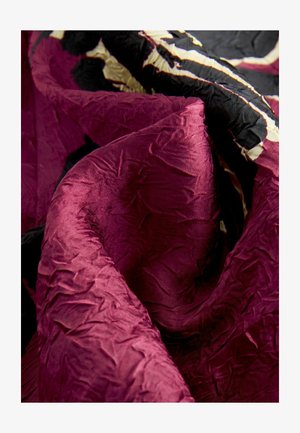 Zúzott bársonyanyag mély burgundi színben, fekete és krémszíni kiegészítőkkel, gyűrött textúrával és sima fényű felülettel.