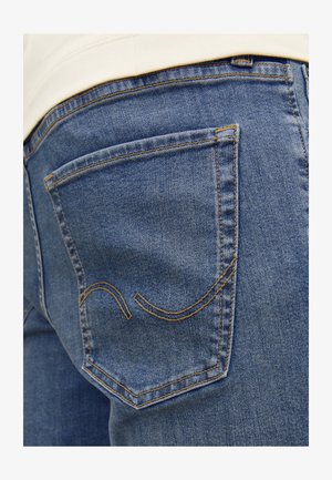 Hellblaue Jeans aus Denim haben ein gewölbtes Taschendesign auf der Rückseite mit gelben Nähten. Der Stoff hat eine glatte Textur und ein abgetragenes Aussehen.