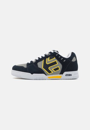 Pantofi de skateboard navy și gri cu un logo galben, șireți albi, tălpi din cauciuc și accente din piele intoarsă. Prezintă un design low-top și materiale respirabile.