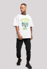 Balta kokvilnas T-krekls ar krāsainu "Rick and Morty" grafiku, apvienots ar melnajām baggy biksēm un melniem sporta apaviem.