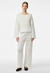 Conjunto de ropa de lounge a rayas blancas que incluye una blusa corta de manga larga y pantalones de pierna ancha en tejido texturizado, combinados con zapatos oscuros.
