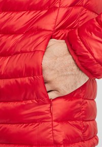 Chaqueta de plumas roja con acolchado horizontal, que cuenta con un bolsillo con cremallera y un suave forro interior. Tejido ligero y texturizado.