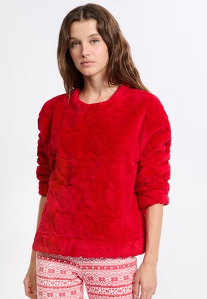 Pullover in pelliccia sintetica rossa con un motivo a forma di cuore testurizzato, dotato di scollatura a girocollo e maniche lunghe. Abbinato a pantaloni con motivo rosso e bianco.