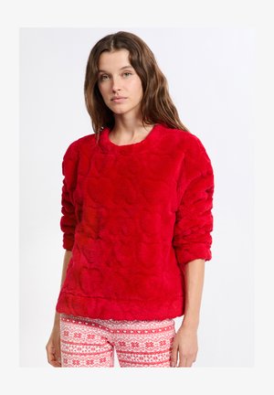 Pullover in pelliccia sintetica rossa con un motivo a forma di cuore testurizzato, dotato di scollatura a girocollo e maniche lunghe. Abbinato a pantaloni con motivo rosso e bianco.