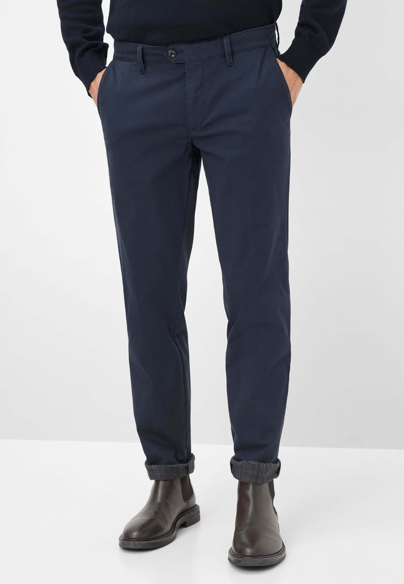 Chinos bleu marine fabriqués en tissu mélangé de coton, avec une coupe classique, des poches avant et des ourlets retroussés révélant un motif à carreaux.