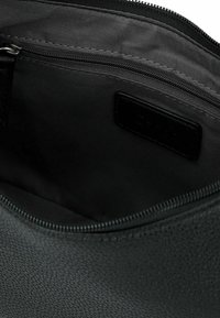 Zwarte handtas interieur met textuur, voorzien van een ritsvak, gladde stof voering en leren label. Ritsafsluiting aan de bovenkant.