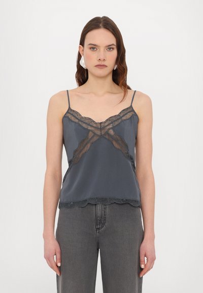 Camisole en satin gris avec des détails en dentelle, fines bretelles, ourlet festonné et accents transparents, associée à un jean en denim gris taille haute.