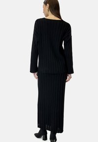 Zwart geribd gebreide trui en lange rok set. Heeft lange mouwen, een brede halslijn en een gestructureerde afwerking met een licht losse pasvorm.
