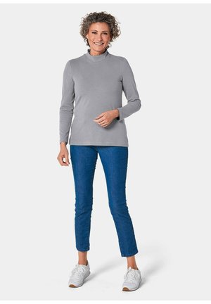 Grijze longsleeve coltrui gecombineerd met blauwe jeans en witte sneakers. De stof lijkt zacht met een gladde textuur.