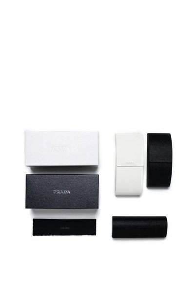 Deux étuis à lunettes Prada en noir et blanc avec des boîtiers de marque assortis et un chiffon de nettoyage noir sur fond blanc.