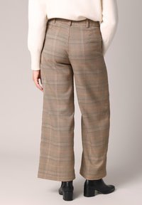 Pantalon à carreaux en beige, marron et noir avec une coupe ample. Présente une taille haute et une coupe ajustée, associé à des bottes noires à talons.