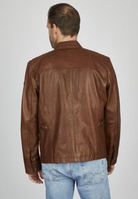 Braune Lederjacke mit glatter Textur, ausgestattet mit einem klassischen Kragen und seitlichen Knöpfen, kombiniert mit hellblauen Jeans.