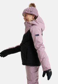 Roze en zwarte geïsoleerde jas met een capuchon, voorzien van een doorgestikt ontwerp. Gecombineerd met zwarte handschoenen en een gestructureerde roze gebreide muts met een pompon.