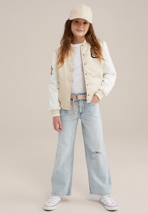 Giacca bomber beige e bianca con chiusura a bottoni, dettaglio a stella nera, abbinata a jeans a gamba larga azzurri e sneakers bianche.