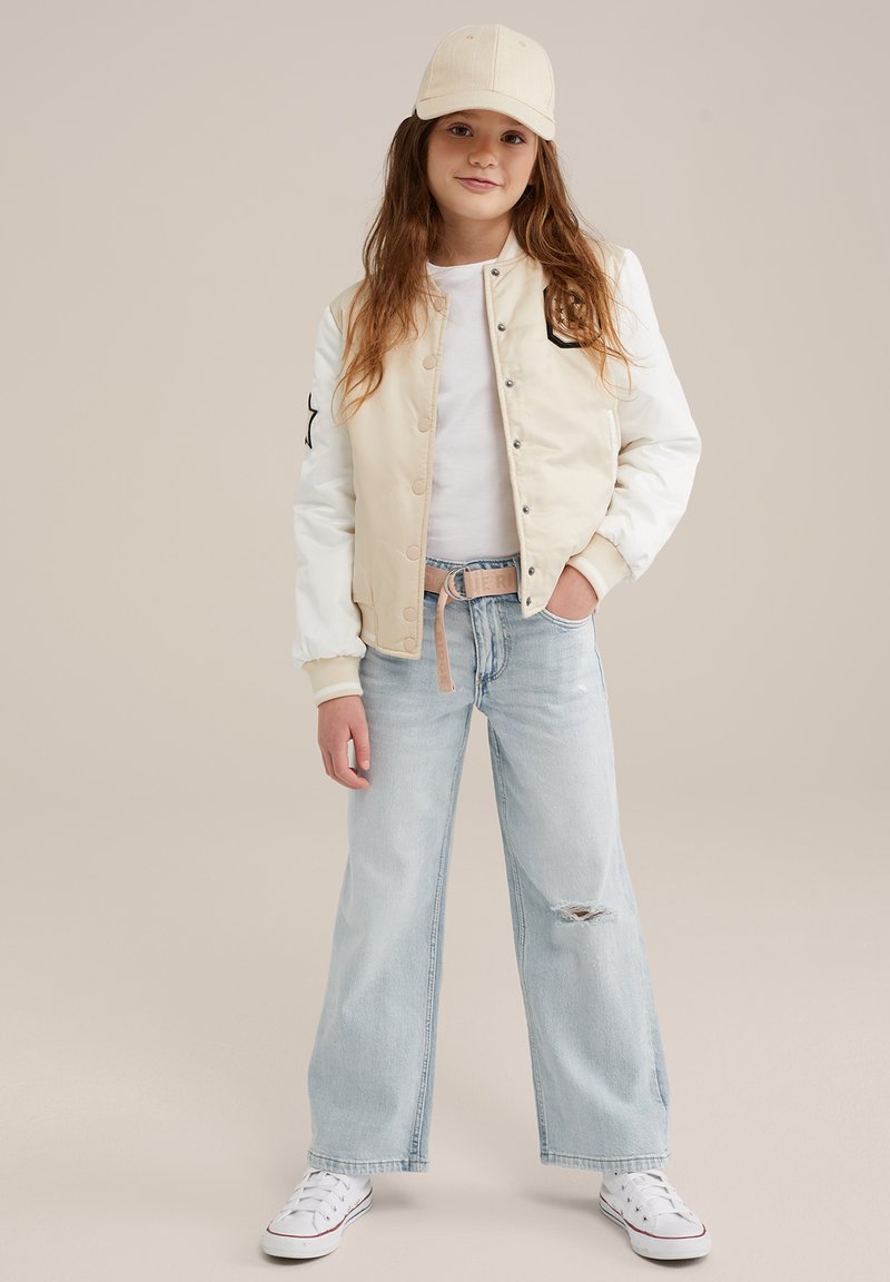 Bežinė ir balta bomber tipo striukė su snap užsegimu, juoda žvaigždutė, derinama su šviesiai mėlynomis plačiomis kelnėmis ir baltomis sportinėmis bateliais.